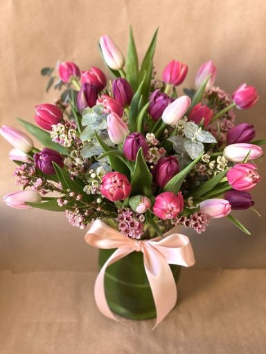 A vibrant bouquet of pink and purple tulips with greenery and a satin ribbon.