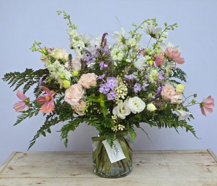 A vibrant bouquet of mixed flowers in a glass vase, featuring pink, white, and purple blooms.