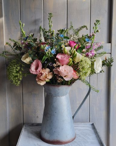 A vintage metal pitcher filled with a variety of colourful flowers.